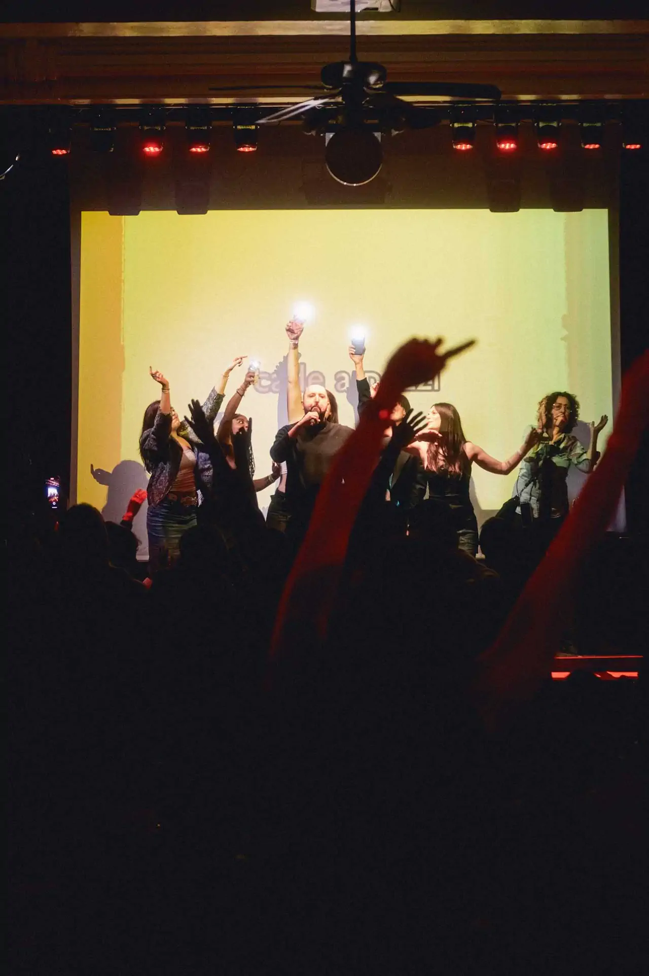 People chanting in front of a crowd, with a projected light behind, in a dark theater. People chanting in front of a crowd, with a projected light behind, in a dark theater.