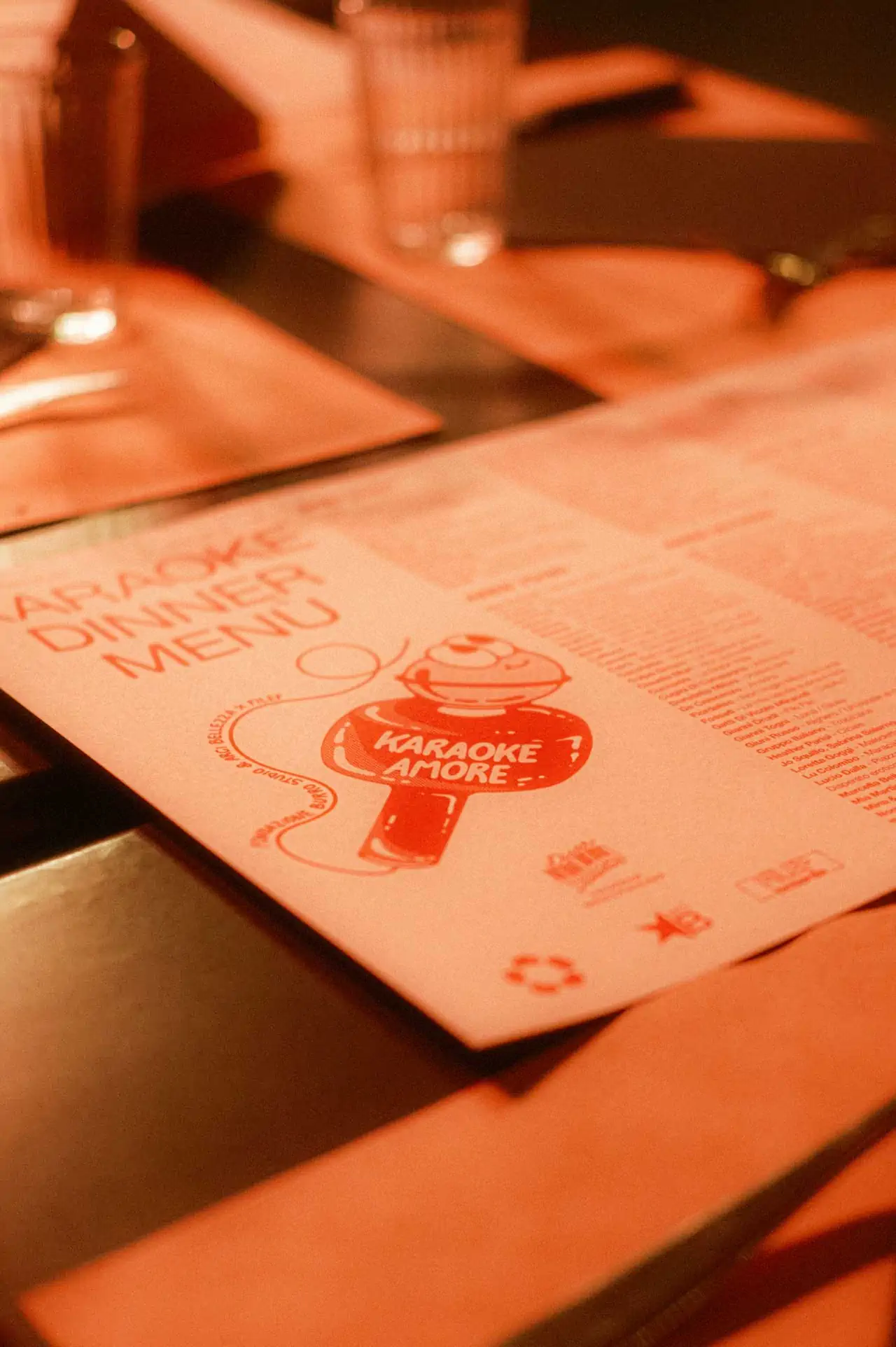 Detail of a white light cardboard paper menu printed in orange, which is laid on a dinner table, in a soft light. Detail of a white light cardboard paper menu printed in orange, which is laid on a dinner table, in a soft light.